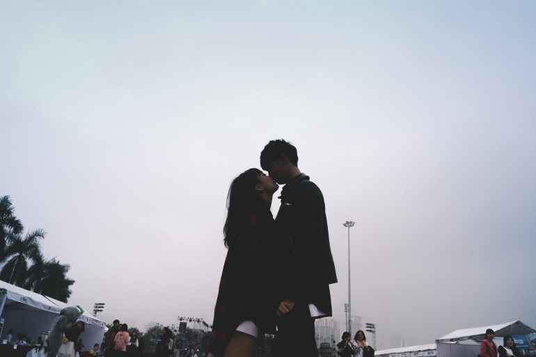 couple kissing together standing near people