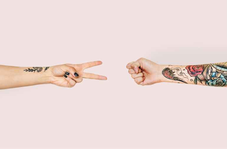 person with tattoo playing paper scissor and stone