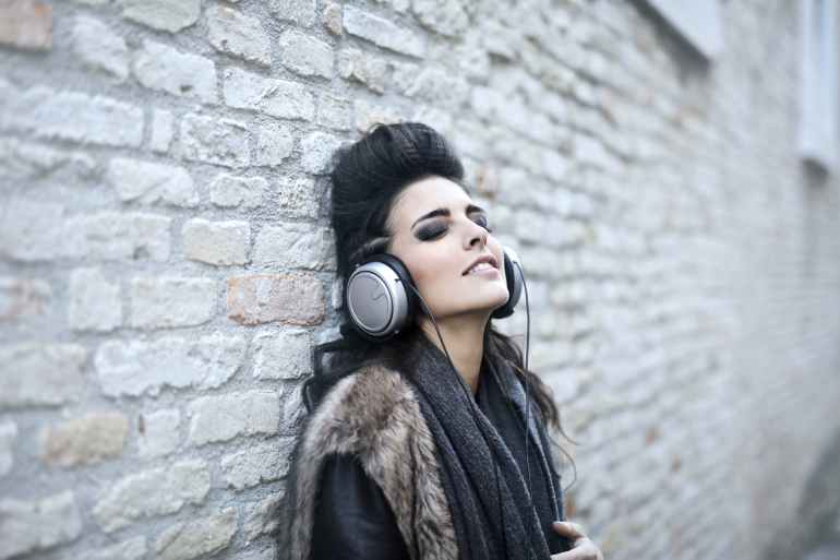 informal young woman listening to music near grunge wall
